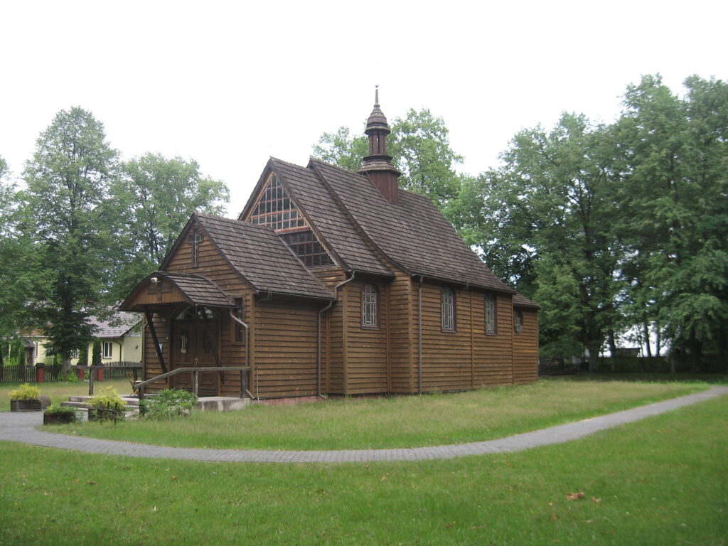 Drewniany kościół z niewielką wieżyczką. Na pierwszym planie zielona łąka