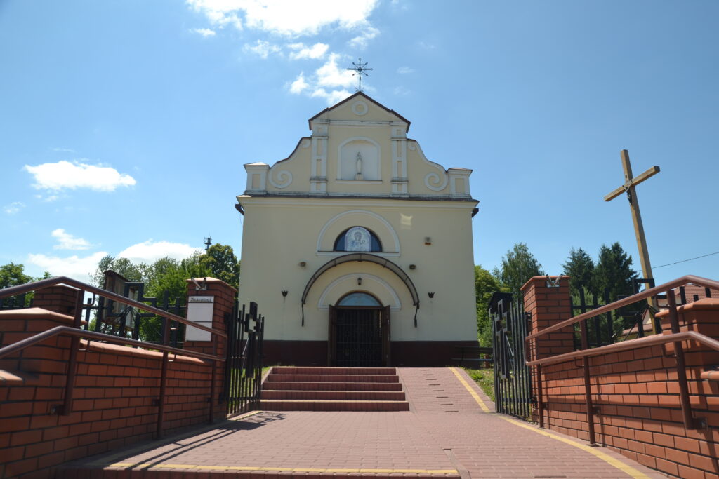 Jasny fronton kościoła, drewniane brązowe drzwi nad nimi Matka Boska Częstochowska. Na szczycie metalowy krzyż