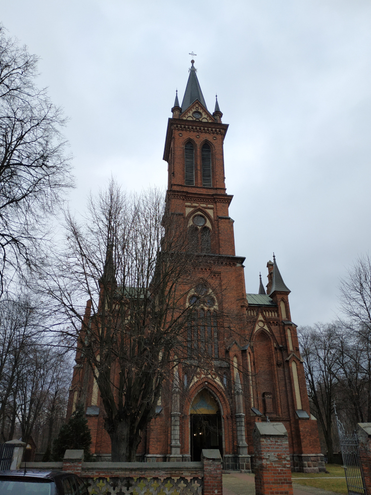 Wysoki kościół zbudowany z czerwonej cegły. Wysokie wejście, kilka okrągłych okien.